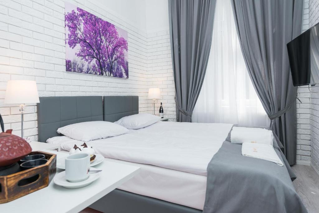 Bright double bed in white brick room with purple tree artwork, gray curtains, tea and cup.