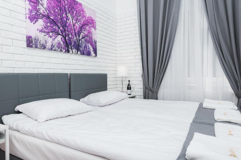 Neatly made bed with gray headboard, folded towels, purple tree artwork and sheer curtains.