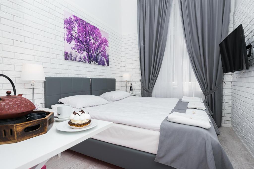 Bright hotel bedroom with double bed, purple tree artwork, tea set and dessert on table.