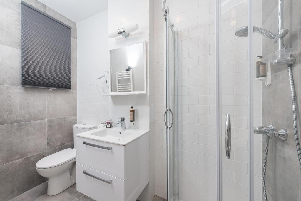 Small bathroom angle showing closed gray window blind, toilet, vanity, glass shower enclosure