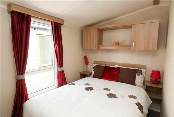a bedroom with a bed with red curtains and a window at Pine drive in Mablethorpe