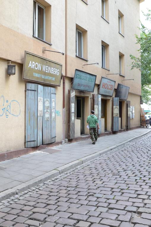 Person in green hoodie walking past shuttered storefronts and aged signage on cobblestone sidewalk.