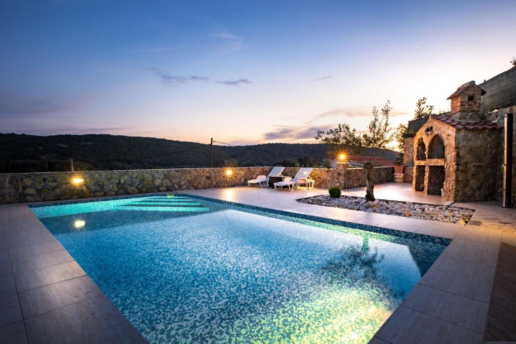 a swimming pool in front of a house with a sunset at Apartments Bajcic in Rab