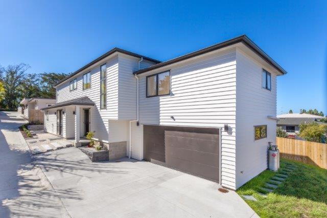 a white house with a garage in a driveway at Stunning Stay In Glen Eden Auckland in Auckland