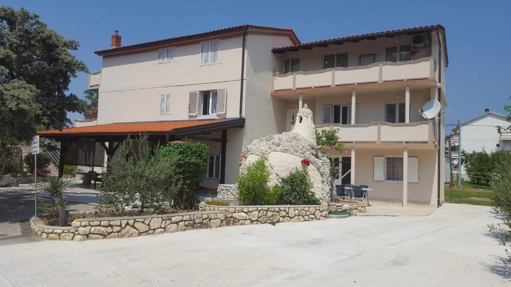 uma grande casa branca com uma estátua em frente em Apartments Ribica em Rab