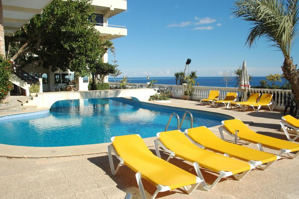 a swimming pool with yellow lounge chairs and the ocean at Hotel Masa International in Torrevieja