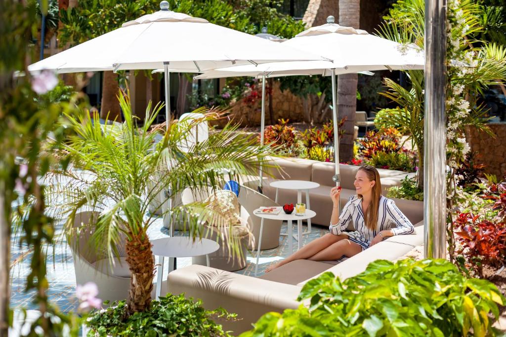 a woman sitting on a couch under an umbrella in a garden at MUR Faro Jandia Fuerteventura & Spa in Morro del Jable