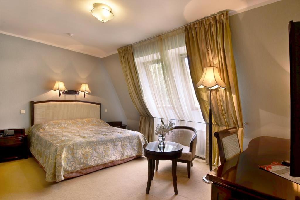 a bedroom with a bed and a table and a window at Greenway Park Hotel in Obninsk