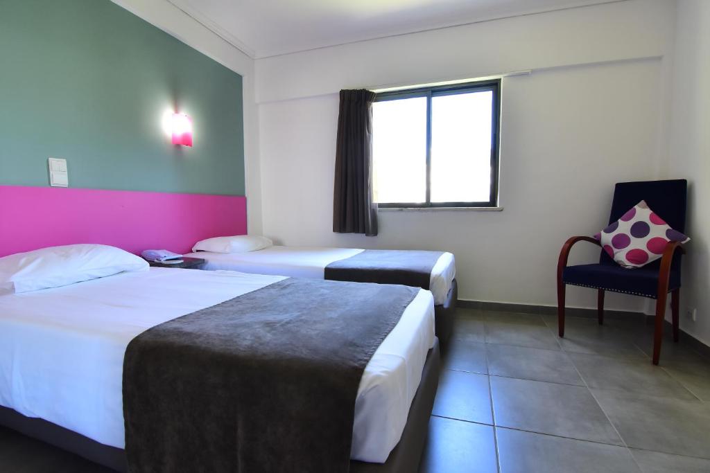 a hotel room with two beds and a chair at Bayside Salgados in Albufeira