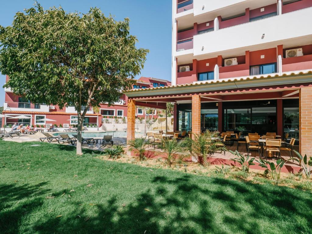 a building with tables and chairs and a tree at Topazio Vibe Beach Hotel & Apartments - Adults Friendly in Albufeira