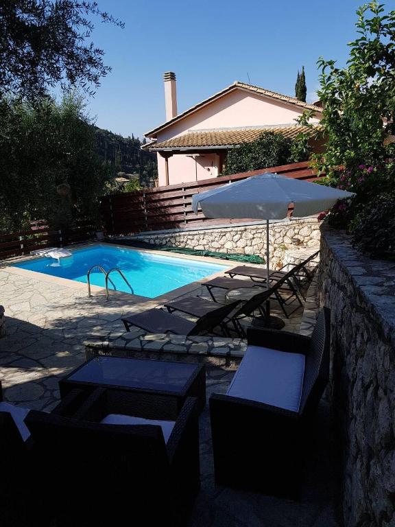 a pool with chairs and an umbrella next to a house at Evridiki's Villas in Agios Nikitas