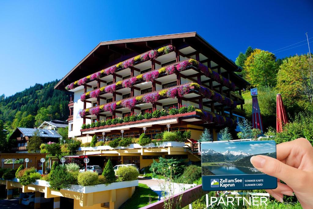 a person taking a picture of a building with flowers at ALPIN- Das Sporthotel - SKI IN SKI OUT cityXpress, SUMMERCARD INCLUDED in Zell am See