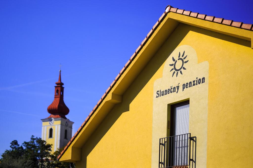 un edificio amarillo con una aguja y una torre de reloj en Slunečný Penzion, en Tasovice