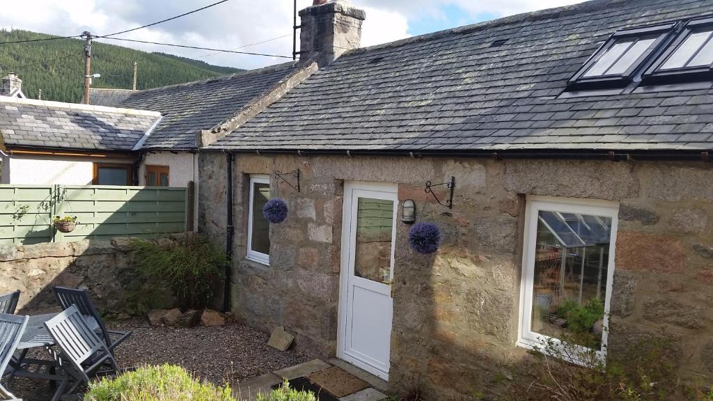 um chalé de pedra com uma porta branca em Fairdene Cottage em Ballater