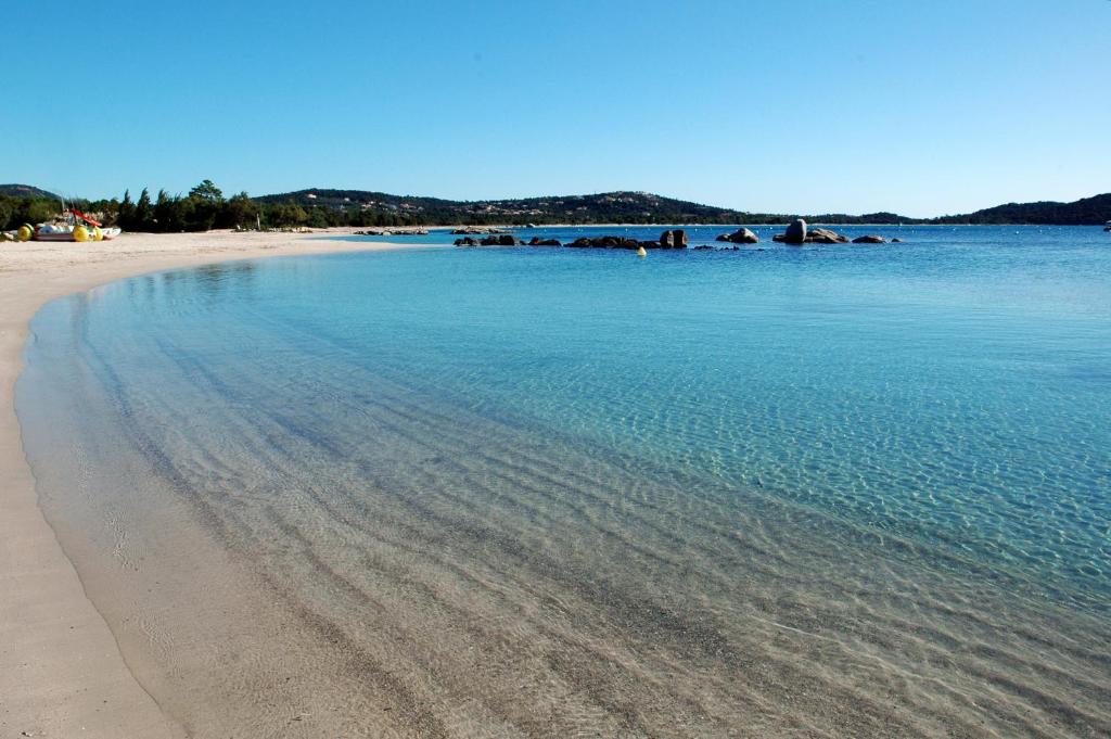 una spiaggia con acqua blu e rocce in lontananza di Cala di Sole Lecci a Porto Vecchio