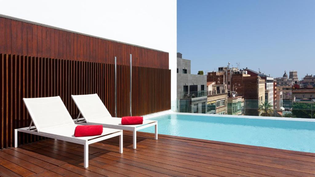 einen Balkon mit 2 Stühlen und einem Pool auf einem Gebäude in der Unterkunft Condes de Barcelona in Barcelona