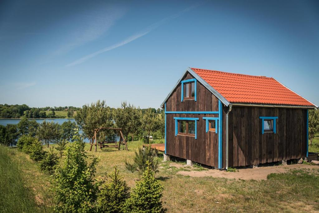 una pequeña casa de madera con techo rojo y columpio en Warmińska Chata, en Kierzliny