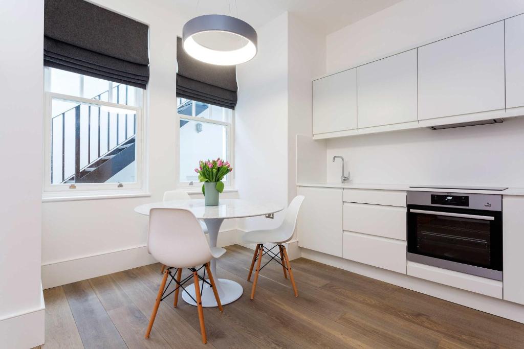 a kitchen with white cabinets and a table and chairs at Veeve - Contemporary Studio in Swiss Cottage in London