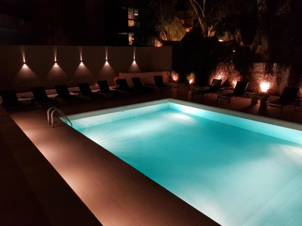uma piscina à noite com cadeiras à volta em Athens coast hotel em Atenas
