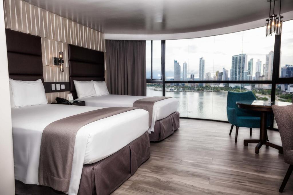 two beds in a hotel room with a view of the city at Plaza Paitilla Inn in Panama City