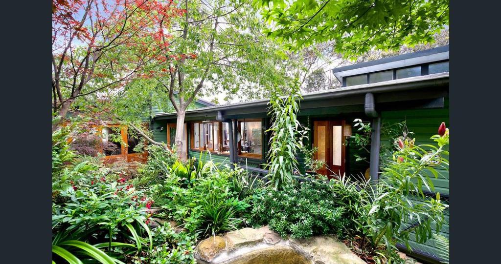 una casa verde con un jardín delante de ella en The Black Cockatoo - Secret Garden Treetops Home, en Katoomba