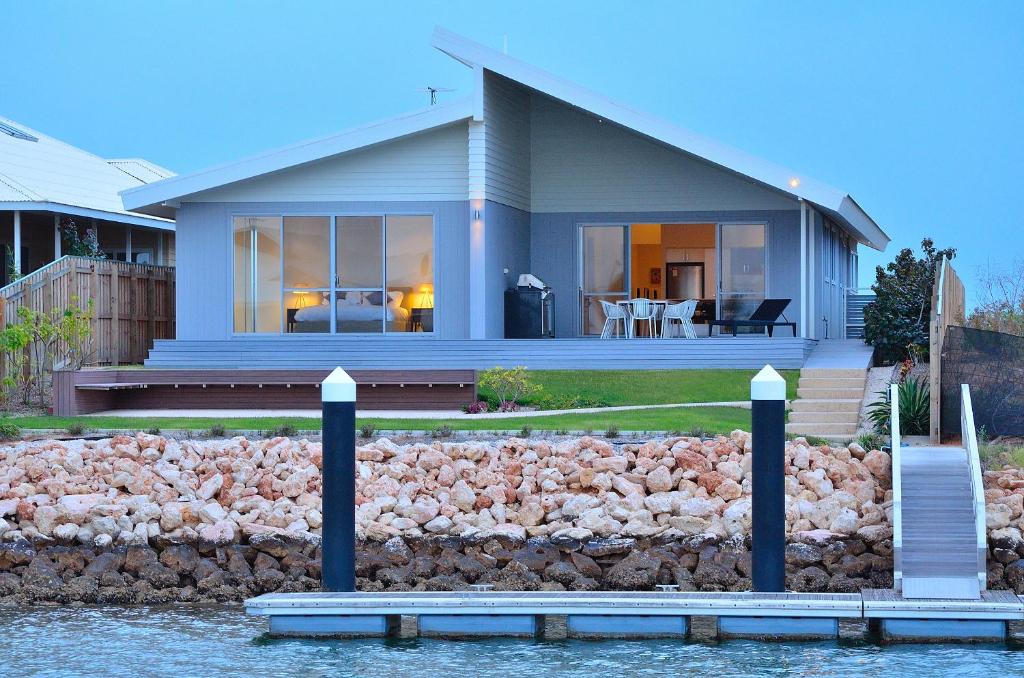 a house on the water with a rock wall at The Carnarvon Luxury Canal Home in Carnarvon