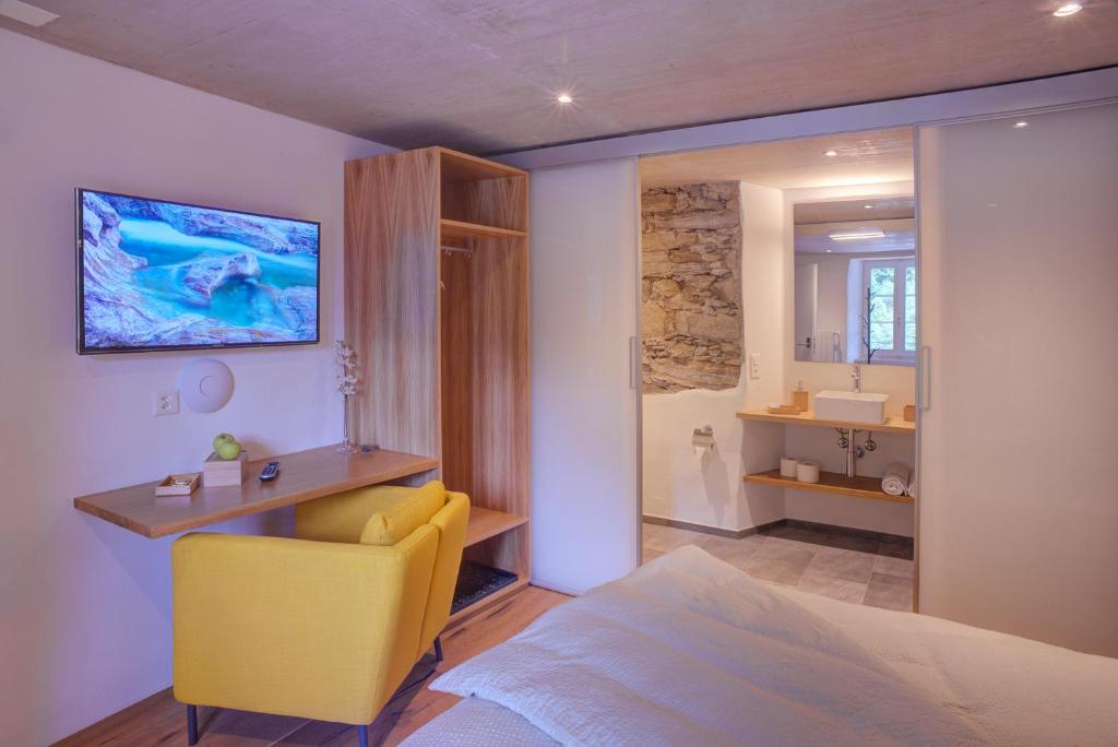 a bedroom with a yellow chair and a bathroom at MyVerzasca Resort Ai piee in Brione