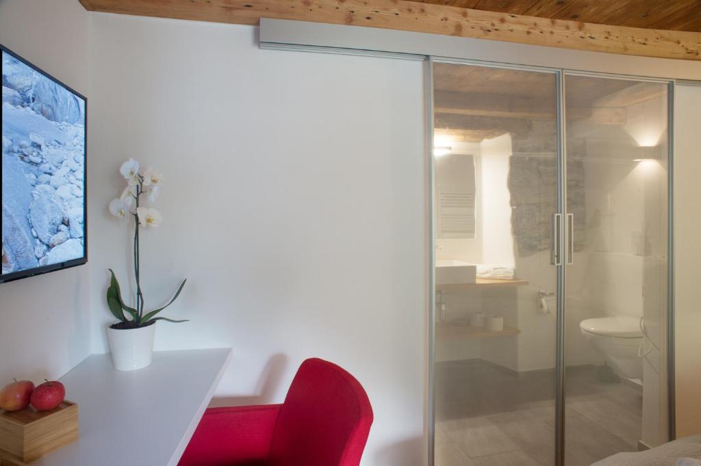 a bathroom with a glass shower and a red chair at MyVerzasca Resort Ai piee in Brione