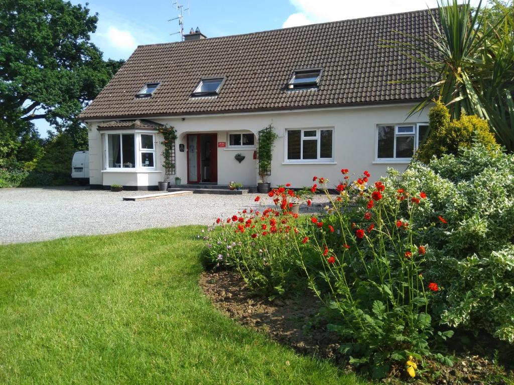 a white house with red flowers in the yard at Twin Oaks Bed & Breakfast in Kilkenny