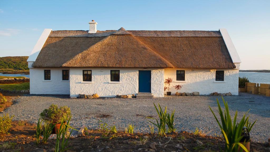 an old house with a thatched roof on a beach at BaySide Cottage in Canower
