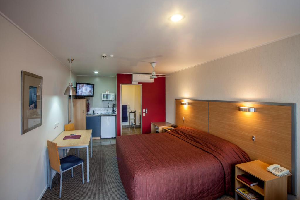 a bedroom with a bed and a desk and a kitchen at Landmark Manor in New Plymouth