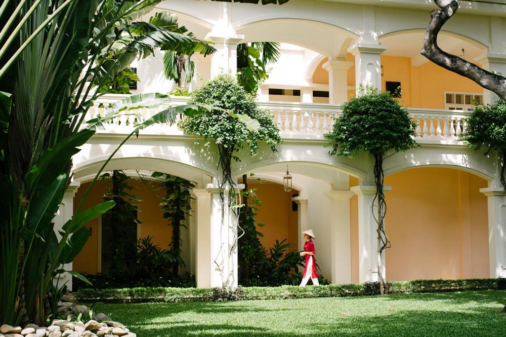 a woman in a red dress walks in front of a building at Anantara Hoi An Resort in Hoi An