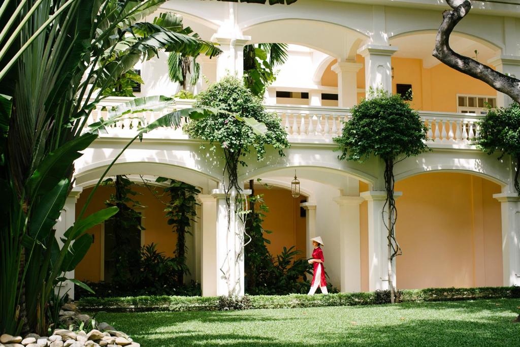 Una mujer vestida de rojo camina delante de un edificio en Anantara Hoi An Resort, en Hoi An