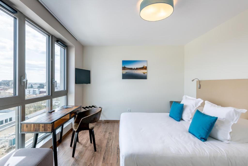 1 dormitorio con 1 cama, escritorio y ventanas en All Suites Bordeaux Marne – Gare Saint-Jean en Burdeos