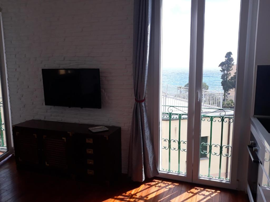 a living room with a television and a balcony with the ocean at House Orizzonte - Casa Bianca in Genoa