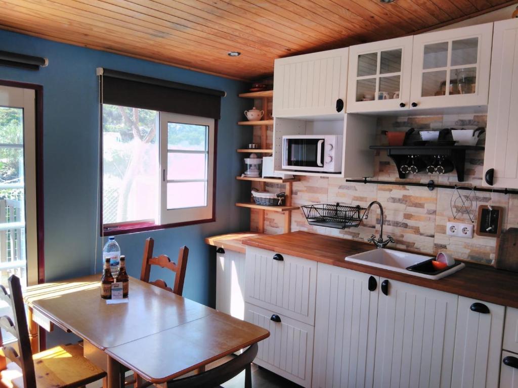 cocina con armarios blancos, mesa y ventana en A Casinha da Baía en Porto Covo