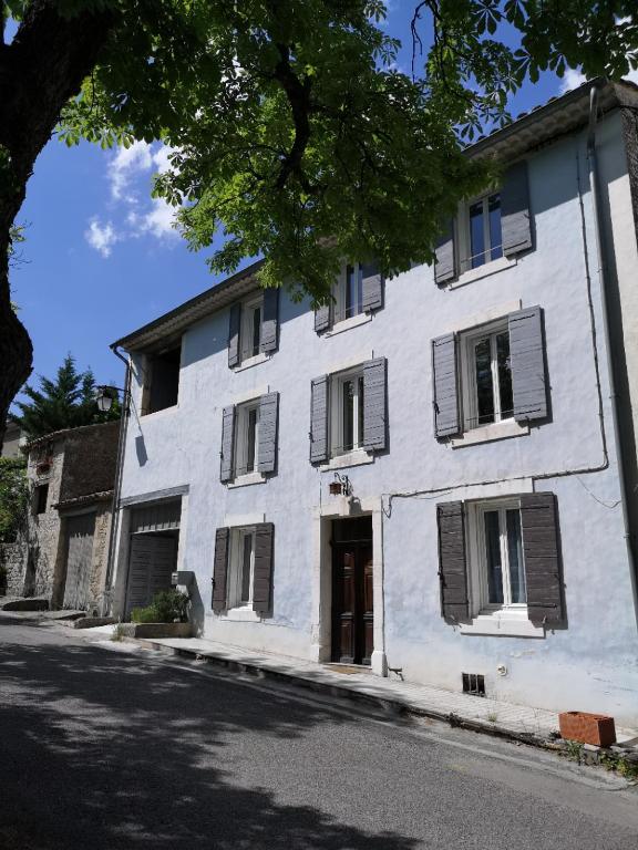 un bâtiment blanc avec des fenêtres à volets sur une rue dans l'établissement La maison Bleue, à Céreste