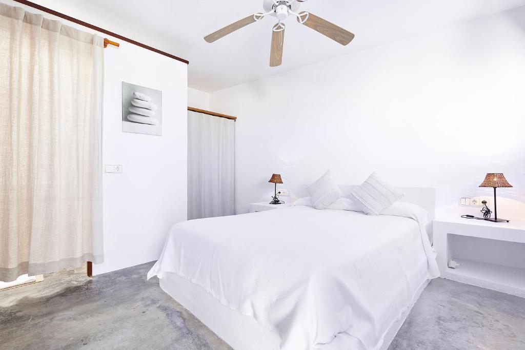a white bedroom with a white bed and a ceiling fan at Can Mares in Cala Tarida