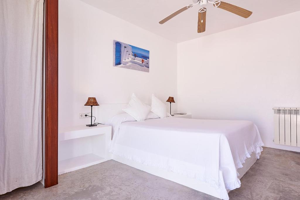 a white bedroom with a white bed and a ceiling fan at Can Mares in Cala Tarida
