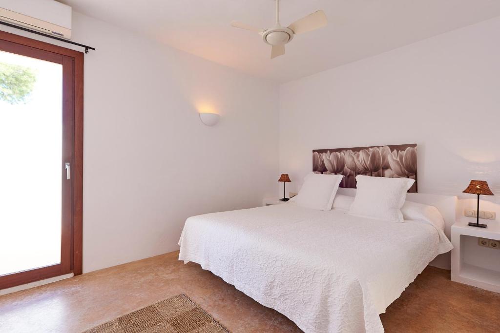 a white bedroom with a white bed and a window at Can Mares in Cala Tarida