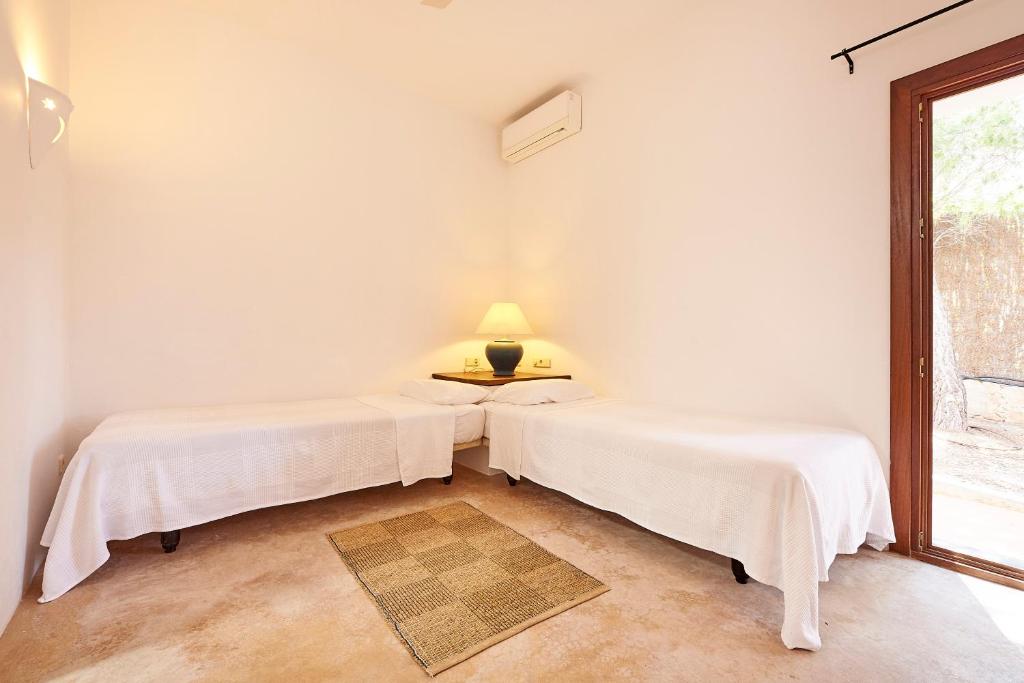 two beds in a white room with a window at Can Mares in Cala Tarida