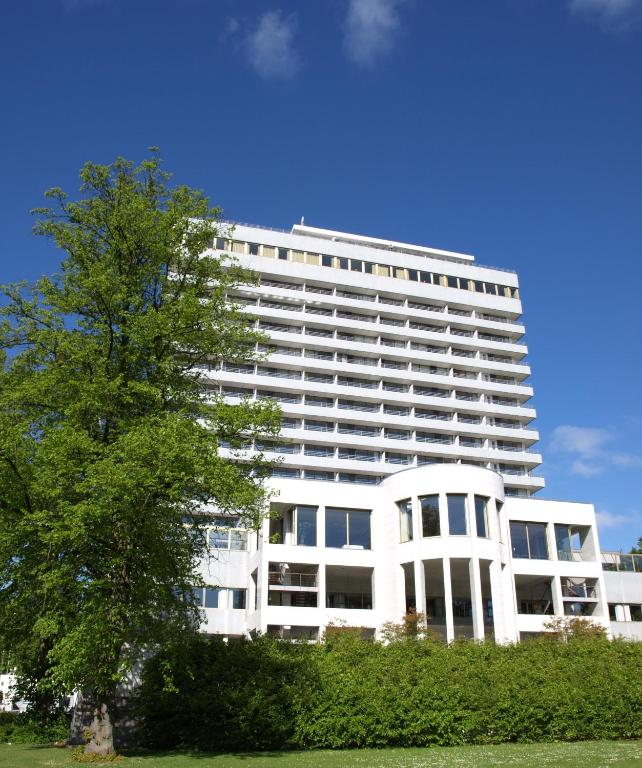 Un edificio blanco con un árbol delante. en Comwell Hvide Hus Aalborg, en Aalborg