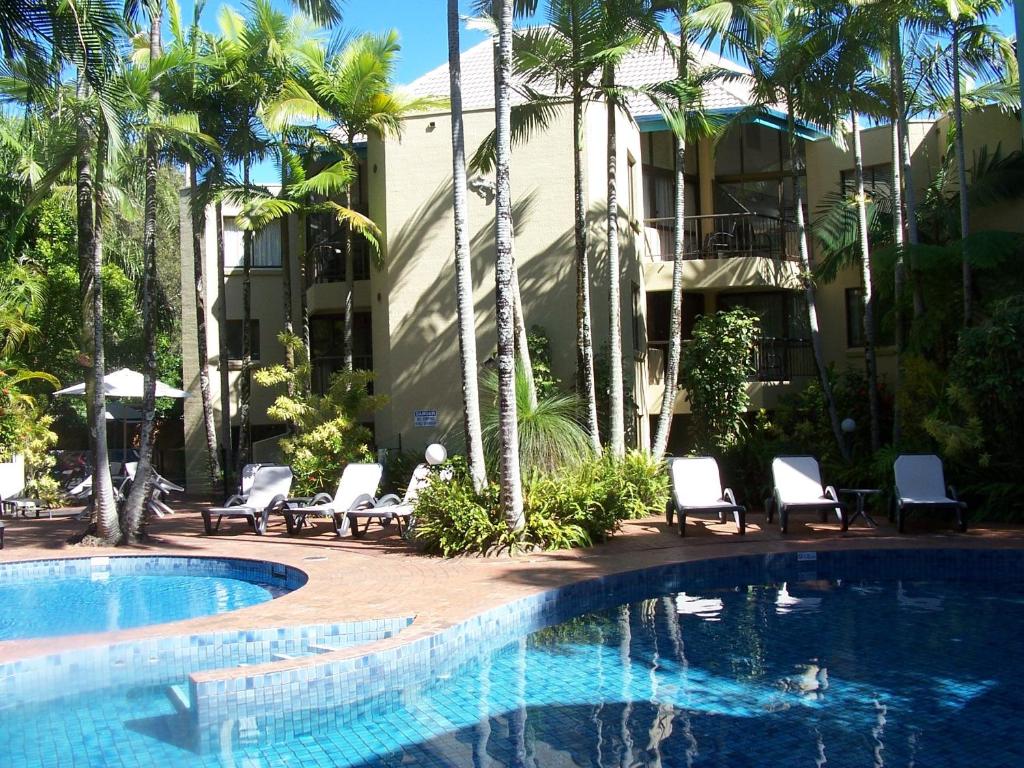 a swimming pool with chairs and palm trees next to a building at Ocean Breeze Resort in Noosa Heads