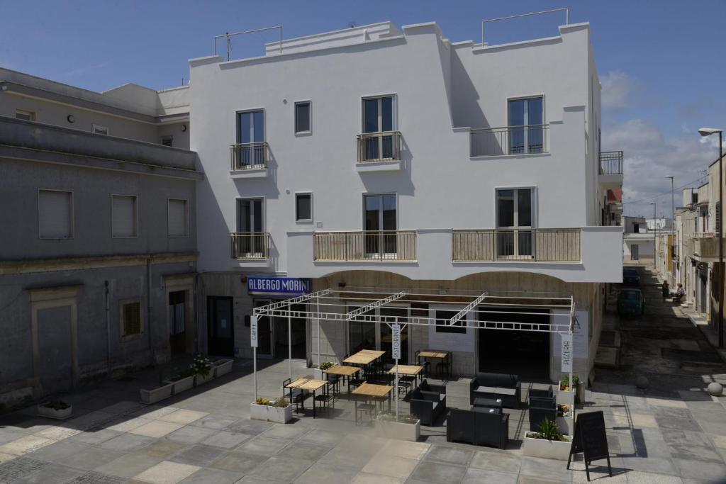 um edifício branco com mesas e cadeiras em frente em Hotel Morini em San Foca
