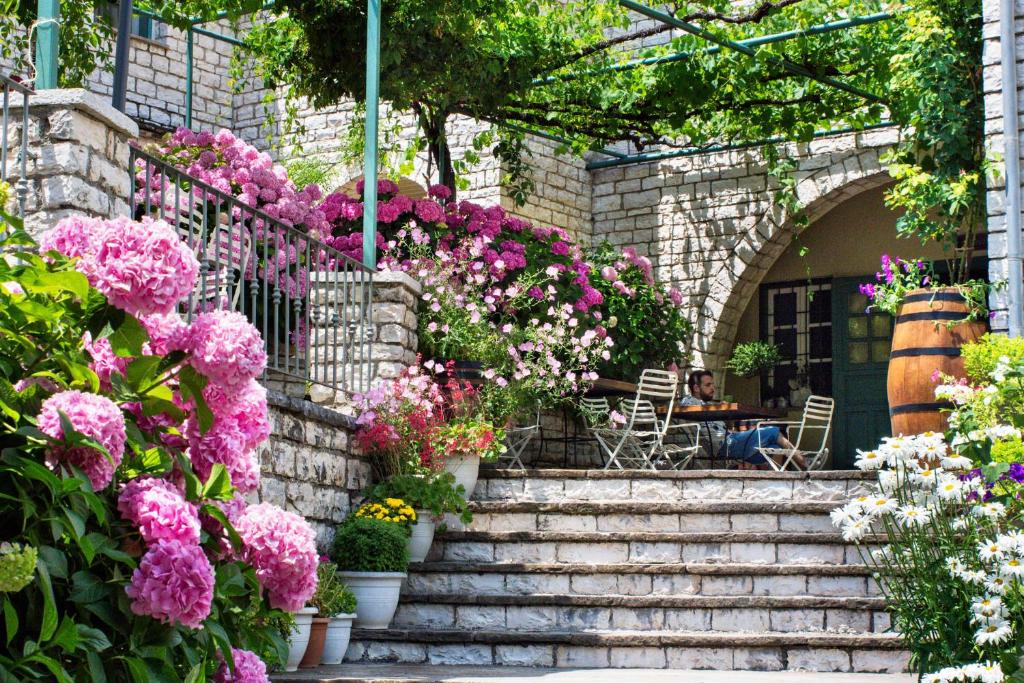 einen Garten mit rosa Blumen und eine Person am Tisch in der Unterkunft Zissis Hotel in Aristi