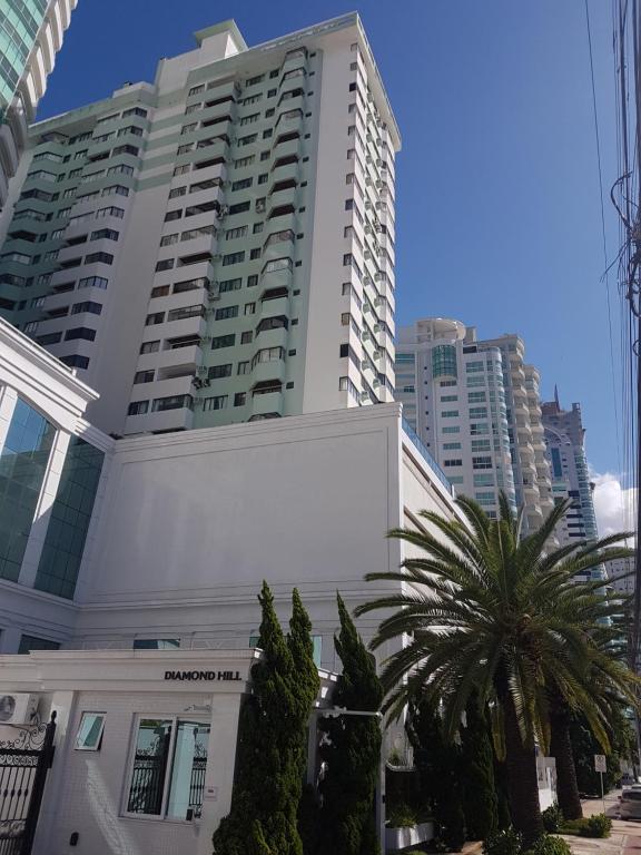 a tall white building with palm trees in front of it at Novo lar Camboriu Park in Balneário Camboriú