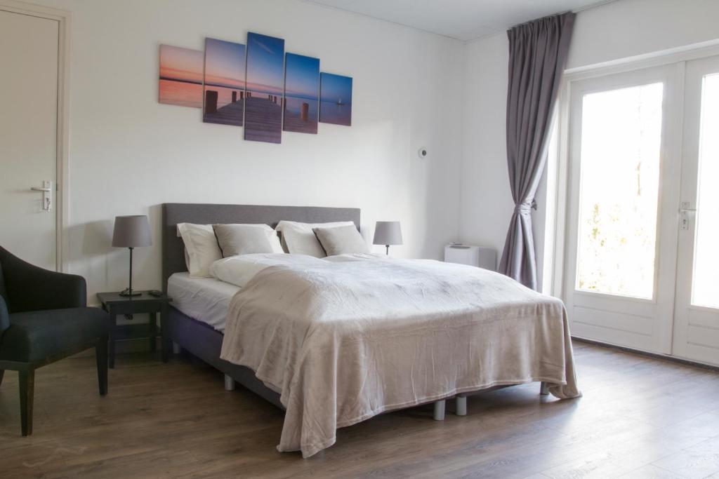 a white bedroom with a large bed and a chair at De Vier Linden in Vierlingsbeek