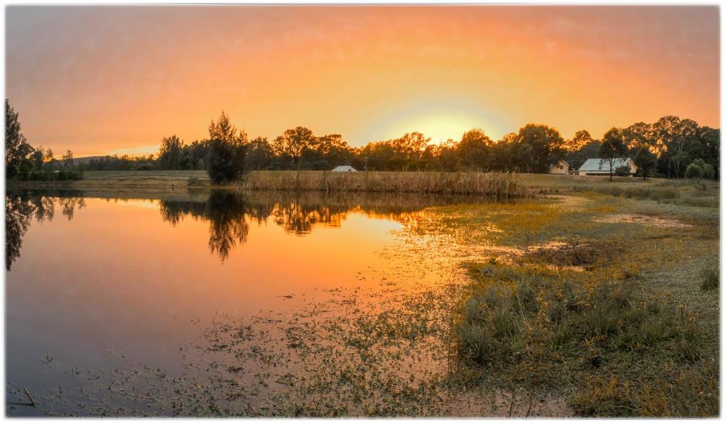 a sunset over a pond with the sun setting in the background at Madigan Wine Country Cottages in Lovedale