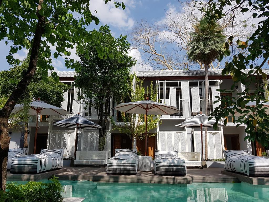 a swimming pool with chairs and umbrellas next to a house at Treevana Club Chiangmai in Chiang Mai