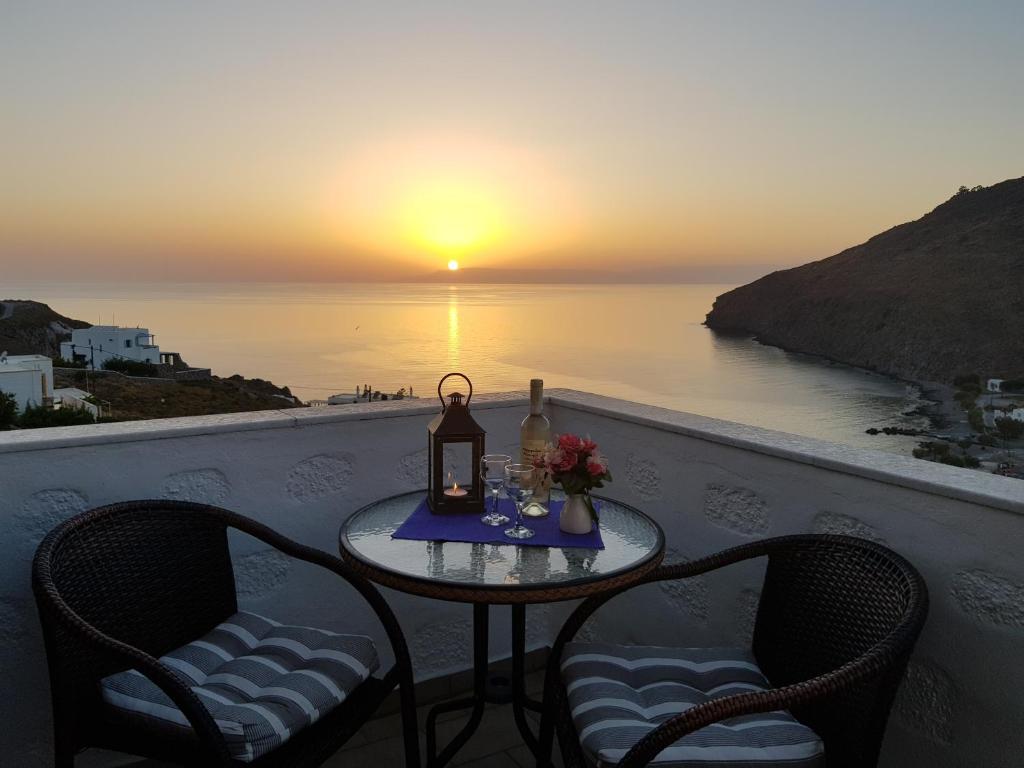 a table with a lamp and two chairs on a balcony with the sunset at Sea View Apartments by Susi & Sofia in Skala